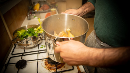 
Close-up on the hands of a man shaking a casserole dish filled with ingredients, above the stove