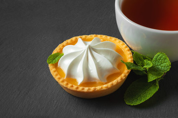 Lemon tart with mint leaves and a cup of tea. Confectionery background on a black slate plate