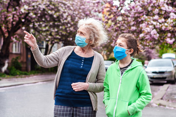 A grandmother with her grandson are walking in respiratory protective masks in an empty city. Danger of infection with coronavirus covid-19. Quarantine. Spring flowering. To point with a finger