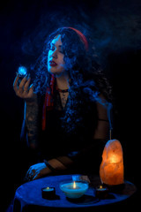 Girl gypsy fortune teller with a red handkerchief at the table with nasty cards candles against a dark background and blue lights