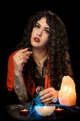 Girl gypsy fortune teller with a red handkerchief at the table with nasty cards candles against a dark background and blue lights