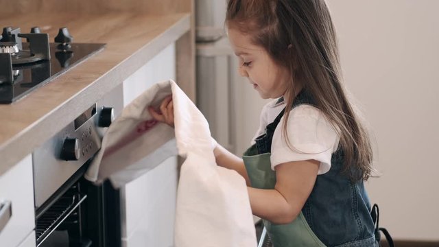 A little girl is baking with her mom. The kid is helping to close a cooker while baking the cookies on Mother's day.