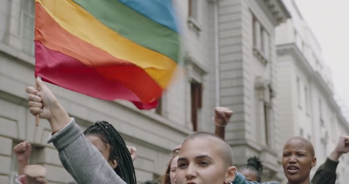 Young people participate in gay pride march. Woman holding a rainbow flag attending a gay parade.
