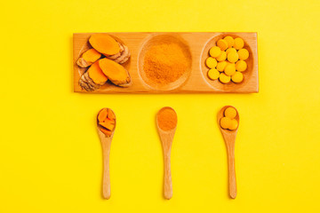 Turmeric in different states: fresh in bottle, pills, powder and cut plant on wooden tray, dry root in wooden bowl.