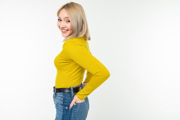 blond girl in a tight-fitting yellow jacket and jeans posing sideways on a white background