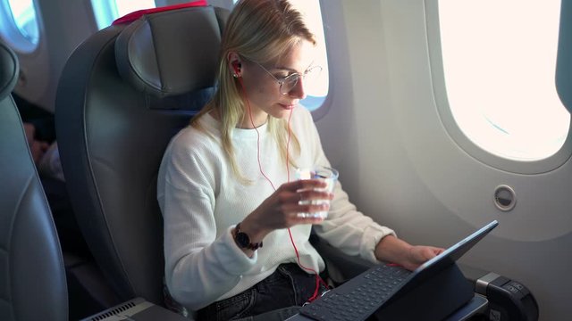Young woman and electronic headphones enjoying intercontinental flight in first class with high speed wifi connection using modern technology for watching movie, comofrtable flight in jetliner
