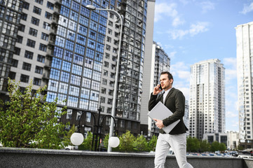 Young businessman is late. A guy with a laptop in smart casual clothes is running down the street and talking on the phone, he is in a hurry for an important meeting