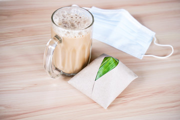 Teh tarik and mask with nasi lemak pack in banana leaf in background, popular breakfast in Malaysia. 