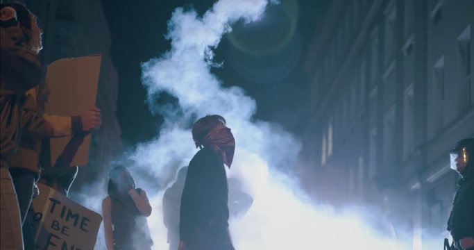 Group of activists participate in the movement to end gun violence. Male protestor throwing the smoke grenade over security force standing on the street at night.
