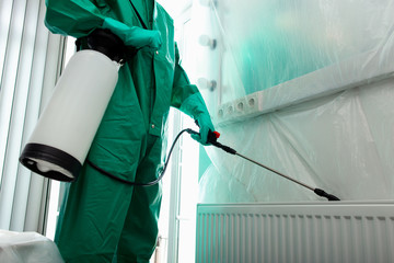 Man in chemical suit getting rid of insects behind the radiator stock photo