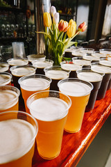 Plastic Beer Glasses on a Wooden Pub Table. A row of plastic beer glasses with a beer on a party.