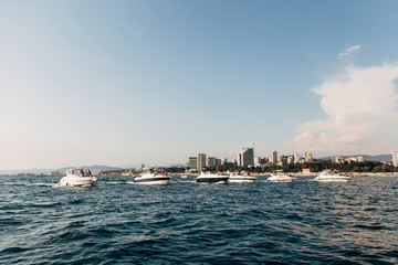 White luxury yachts and boats sail in a row on the open sea against the background of the city