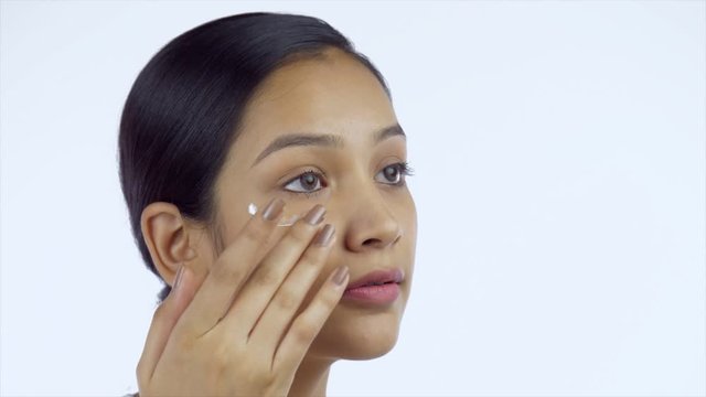 Closeup shot of a beautiful Indian girl with no makeup caring for her facial skin - Skin Care. Portrait of a young female applying skincare cream on her face before going to sleep against the white...
