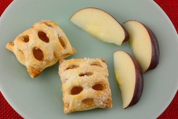 Closeup of two mini apple strudel pastries with three slices of red apple on breakfast plate