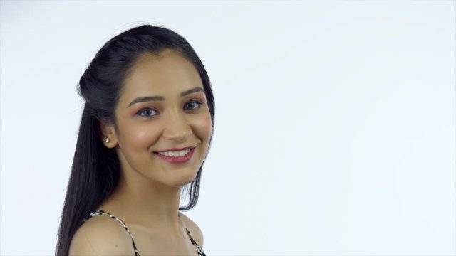 Closeup shot of a beautiful girl removes her glasses and gives a wide toothy smile. Prety Indian female with long straight hair happily turns towards the camera and gives a playful smile - white ba...