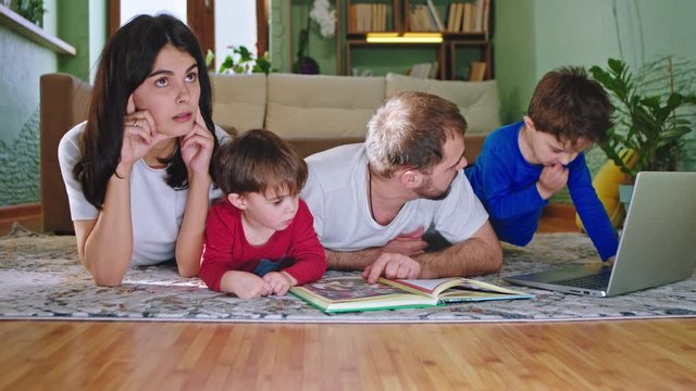 Young mam and dad spending time at home with their two kids they reading books and have a good time together