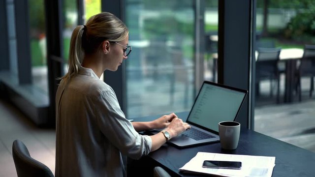 Skilled woman in casual wear sitting in coworking space and working with program code for public website with many functional options, young freelancer typing text information during distance job
