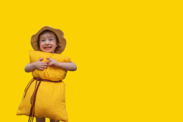 a beautiful little girl with a hat and a yellow pillow on her belly with a strap attached to her belt looks into the camera and smiles at a bright yellow background - a concept of orthopedic comfortab