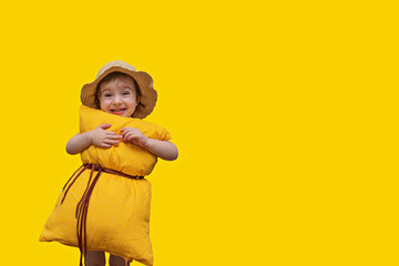 Little girl posing on a yellow background in a pillow instead of a dress and a straw hat. Pillow call. Vivid emotions: happiness, delight, sadness, tomfoolery. Happy childhood