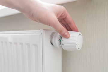 Home central heating system. Woman's hand turns the regulator. House energy efficiency