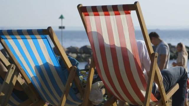 People relaxing on red and white and blue and white striped deckchairs on a British beach in summer