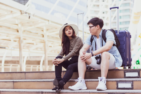 The male and female couples are Asian Thai tourists wearing casual clothes, talking to each other on the stairs, with luggage on the back and a building background.