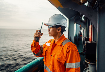 Filipino deck Officer on deck of vessel or ship , wearing PPE personal protective equipment. He speaks to VHF walkie-talkie radio in hands. Dream work at sea - obrazy, fototapety, plakaty