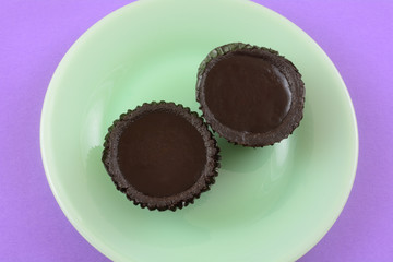 Two dark chocolate tarts with chocolate crusts in paper cups on green dessert plate