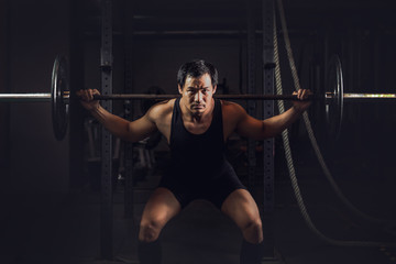 Fototapeta premium asian athletic strong man having workout and bodybuilding with barbells weightlifting backsquat style in gym and fitness center in dark tone