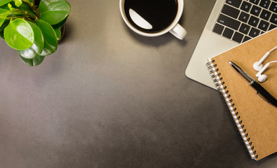Workplace in office with dark grey table. Top view above of laptop with notebook, earphone and coffee. Space creative work of a designer. Flat lay with blank copy space. Business and finance concept.