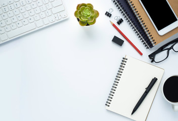 Workplace in the office with a white desk. Top view from above of keyboard with notebook and pen. Space for modern creative work of designer. Flat lay with copy space. Business and finance concept.