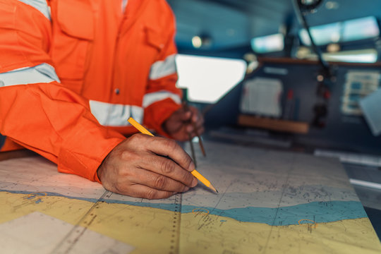 Filipino deck Officer on bridge of vessel or ship wearing coverall during navigaton watch at sea . He is plotting position on chart