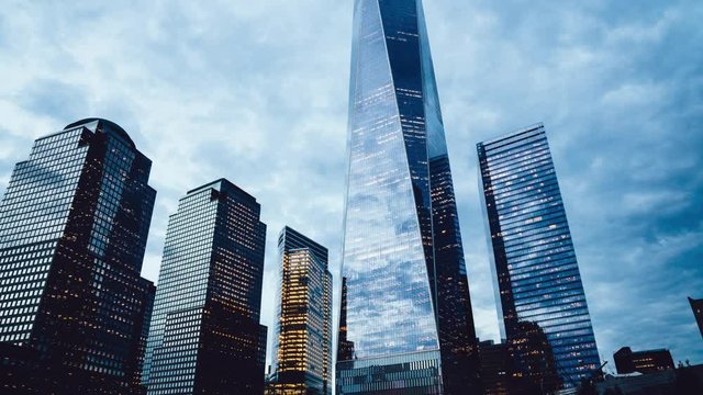Day to night sunset during time lapse effect of American downtown of New York, below view of modern skyscraper buildings and condominium hotels and banks

