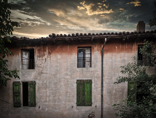 Rundown building with green shutters at sunset under stormy clouds