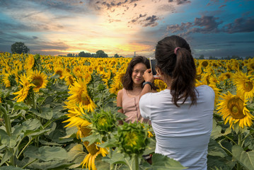 Mother taking photos of daughter in a field surrounded by sunflowers with beautiful sunset