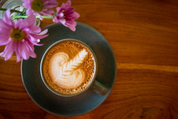 Cup of coffee and flowers on a wooden table. Hot cappuccino with foam
