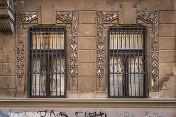 Fototapeta na wymiar Two windows with twisted iron grates on the side of stone building