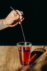 A man hand holding metal straw or stainless straw above a glass of red sweet drink on wooden table.