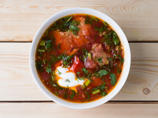 Borsch with sour cream in a white bowl on a wooden background. Top view