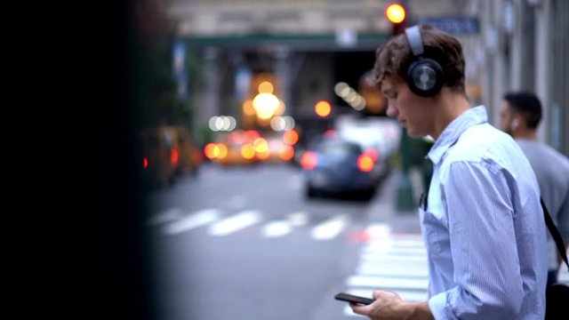 Slow motion of owner in formal apparel walking in metropolitan street and using cellphone for chatting and listening audio book about business success, electronic headphones for noise cancellation
