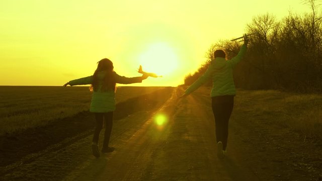 Two girls play with a toy airplane at sunset. healthy Children run on road with an airplane in hand. Silhouette of free children playing airplane. Dreams of flying. concept of a happy childhood.