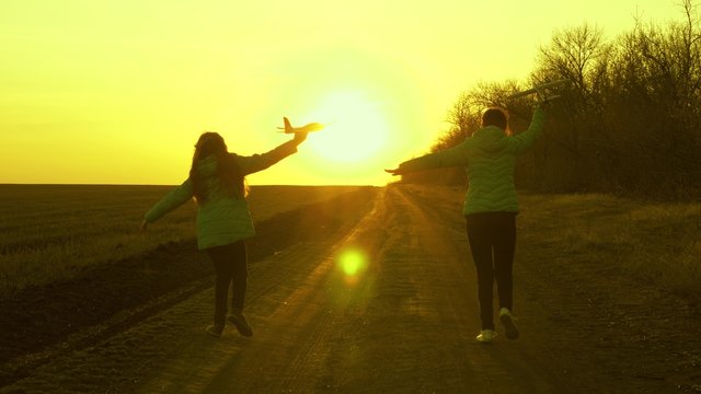 Two girls play with a toy airplane at sunset. healthy Children run on road with an airplane in hand. Silhouette of free children playing airplane. Dreams of flying. concept of a happy childhood.