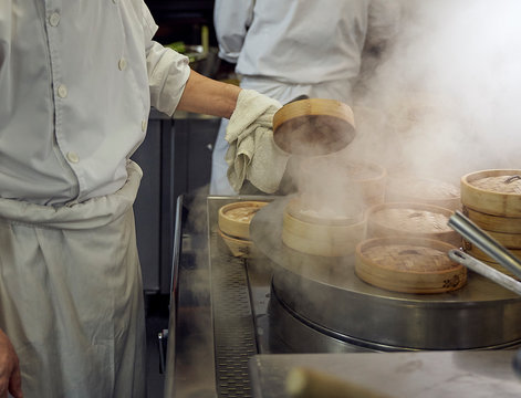 Chef lifts lid off dumpling steamer in a Chinese restaurant kitchen