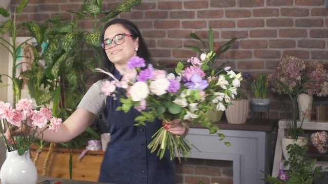 Brunette girl with dark hair in glasses dancing with a bouquet of flowers in her hands. Female smiles and enjoys the flowers donated for Valentine's Day. Woman small business owner joy in success.