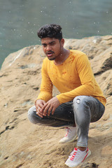 young man model sitting near a river beach in the sun shine