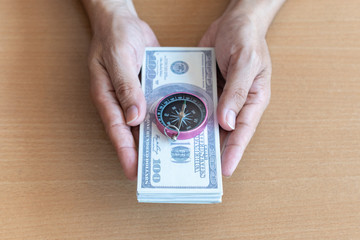 Man hands holding 100 dollar bills and compass on wooden table. Wealth and financial concept