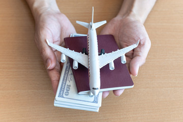 Man hands holding 100 dollar bills and airplane on wooden table. Travel concept