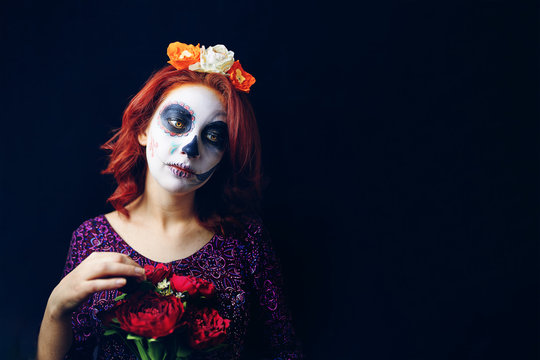 Sad red-haired woman with downcast eyes in day of the dead mask skull face art make-up on a black background. Halloween concept, copy space