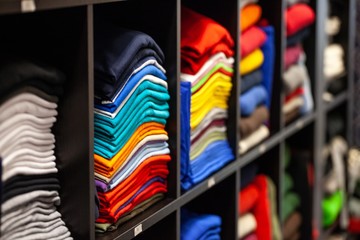 details of clothing and textile on display in clothing store folded, stacked and hanging
