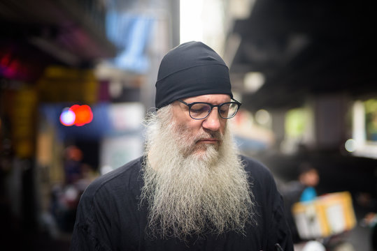 Face of mature bearded hipster man using phone in the city